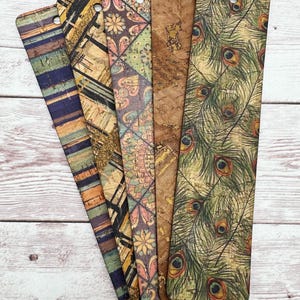 May include: Set of six cork bookmarks with different patterns. The patterns include stripes, geometric shapes, floral designs, and peacock feathers. The bookmarks are all rectangular and have a hole at the top for hanging.