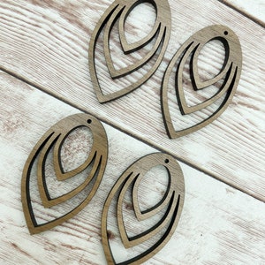 May include: Four wooden earrings with a layered, oval shape. Each earring has three layers, creating a unique and intricate design. The earrings are a light brown color and have a hole at the top for attaching earring hooks.