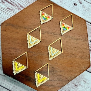 May include: Six triangular earrings featuring gold-tone metal frames and small seed beads. Two earrings have a rainbow pattern, two have a light blue and cream pattern, and two have a bright yellow and cream pattern arranged in a chevron design.