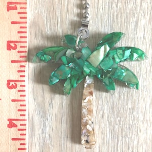 May include: A green and white palm tree fan pull with a silver chain. The palm tree is made of iridescent shell pieces.