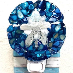 May include: A blue and white sand dollar night light with a white switch. The sand dollar is made of glass and has a textured surface.