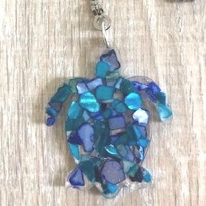 May include: A blue and green sea turtle pendant necklace made of resin with embedded pieces of glass. The pendant is on a silver chain.