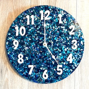 May include: A round clock with a blue and green mosaic background. The clock face has white numbers and hands.