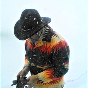 Puede incluir: Una persona con un sombrero negro y una chaqueta estampada de colores con fondo negro. La chaqueta tiene detalles rojos, amarillos y naranjas. La persona est&aacute; de pie en la nieve.