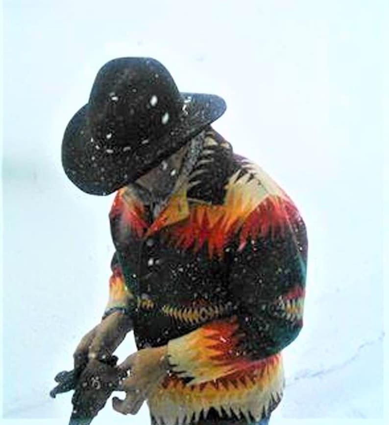 Puede incluir: Una persona con un sombrero negro y una chaqueta estampada de colores con fondo negro. La chaqueta tiene detalles rojos, amarillos y naranjas. La persona est&aacute; de pie en la nieve.