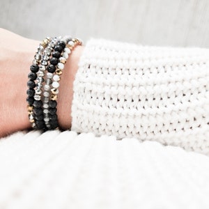 May include: A stack of bracelets with black lava beads, silver beads, and gold beads.