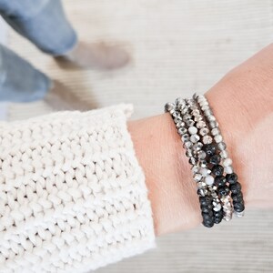 May include: A stack of bracelets with black lava beads, gray and silver glass beads, and clear beads.