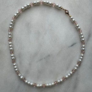 May include: A white pearl necklace with small pink crystal beads.