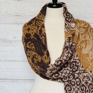 May include: A brown, beige and gold patterned knitted scarf with a gold and crystal brooch.
