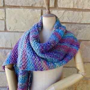 May include: A blue, purple, and green knitted scarf with a fringe. The scarf is draped over a wooden mannequin.