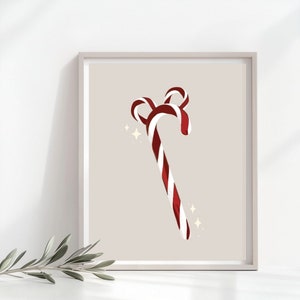 Op de afbeelding: Een ingelijste print met een gestileerd ontwerp van een zuurstok. De zuurstok heeft rode en witte strepen en een gebogen bovenkant. De achtergrond is neutraal en er zijn fonkelende sterretjes, ideaal voor feestelijke decoratie.