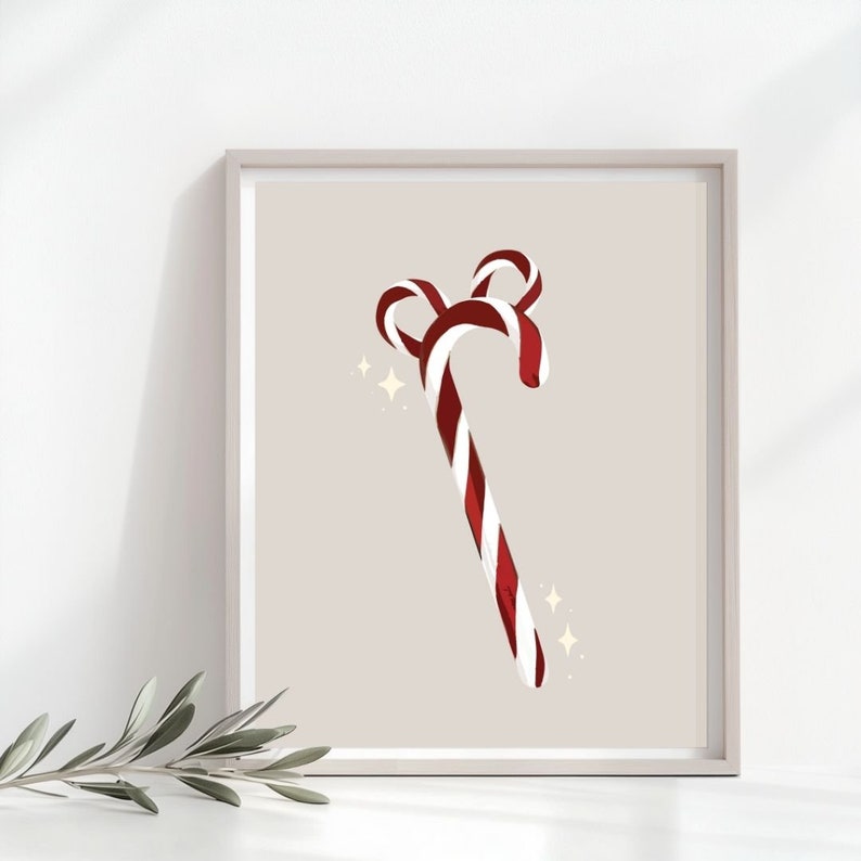Op de afbeelding: Een ingelijste print met een gestileerd ontwerp van een zuurstok. De zuurstok heeft rode en witte strepen en een gebogen bovenkant. De achtergrond is neutraal en er zijn fonkelende sterretjes, ideaal voor feestelijke decoratie.