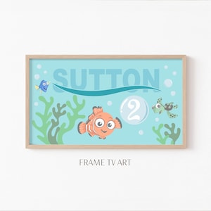May include: A framed print featuring an underwater scene with cartoon characters. The print includes a clownfish, a blue tang, and a sea turtle. The name "SUTTON" is displayed above the characters, with the number "2" in a bubble. The words "FRAME TV ART" are at the bottom.