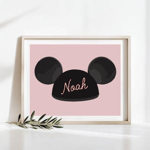 Op de afbeelding: Een roze achtergrond met een zwarte Mickey Mouse orenhoed met de naam Noah in roze op de voorkant.