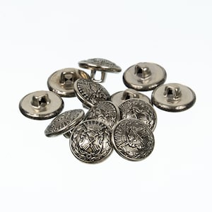 May include: A group of silver-toned buttons with intricate designs. The buttons have a raised, ornate pattern and a shank for sewing.