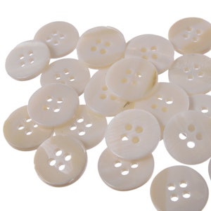 May include: A pile of white, round, four-hole buttons made of mother of pearl.