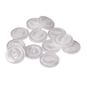 May include: A group of white plastic buttons with two holes each. The buttons are arranged in a pile, with some overlapping.