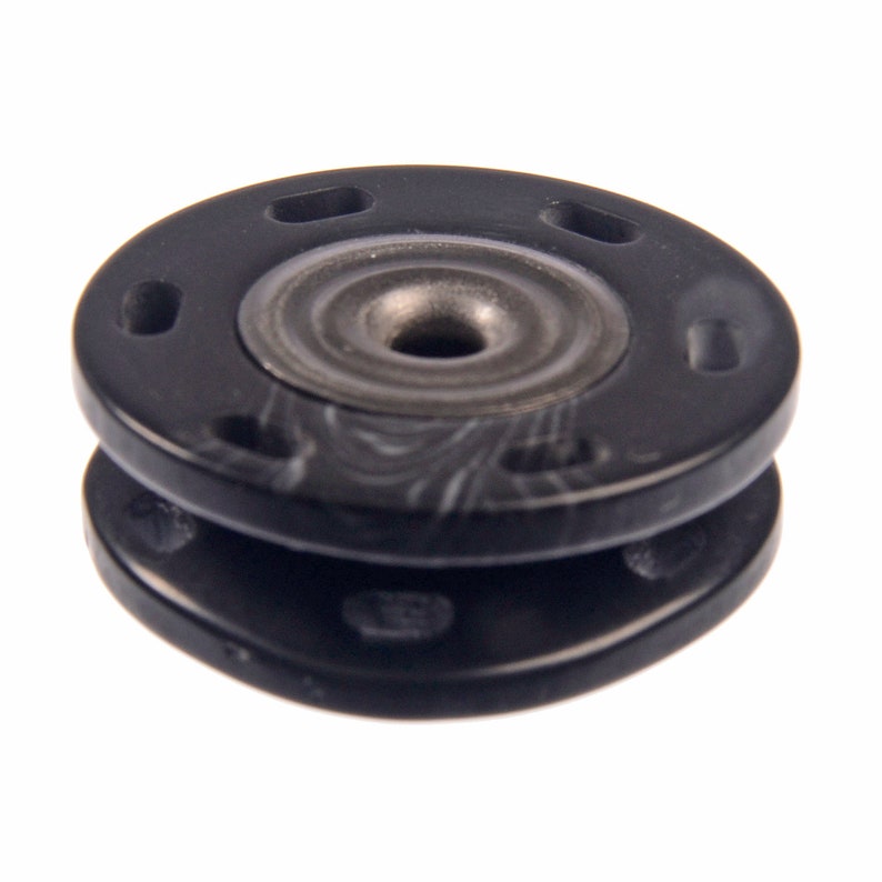 May include: Black plastic snap fastener with a metal center. The fastener has a textured surface and a raised ring around the center.