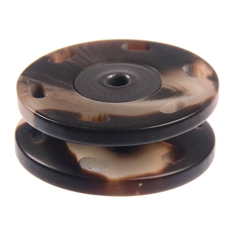 May include: A pair of black and white patterned round buttons with a hole in the center. The buttons are stacked on top of each other.