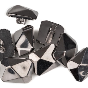 Puede incluir: Un conjunto de botones facetados de color plomo con un diseño geométrico. Los botones tienen varias formas, incluyendo rectangulares y de diamante. Cada botón tiene un vástago en la parte posterior para coser a la tela.