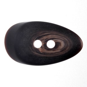 May include: A black and brown oval-shaped button with two holes. The button has a swirl pattern.