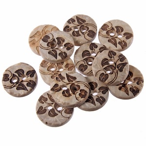 May include: A collection of 10 natural wood buttons with a floral design. The buttons are round and have two holes. The buttons are a light brown color with a darker brown floral design.