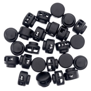 Könnte beinhalten: Eine Gruppe schwarzer Kunststoff-Schiebeverschlüsse mit einem Federmechanismus. Die Verschlüsse dienen zum Sichern von Schnüren, Bändern oder anderen Gegenständen.