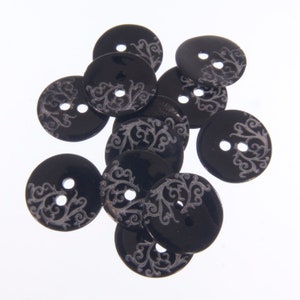 Könnte beinhalten: Eine Gruppe schwarzer Knöpfe mit einem silbernen Wirbelmuster. Die Knöpfe sind rund und haben zwei Löcher.