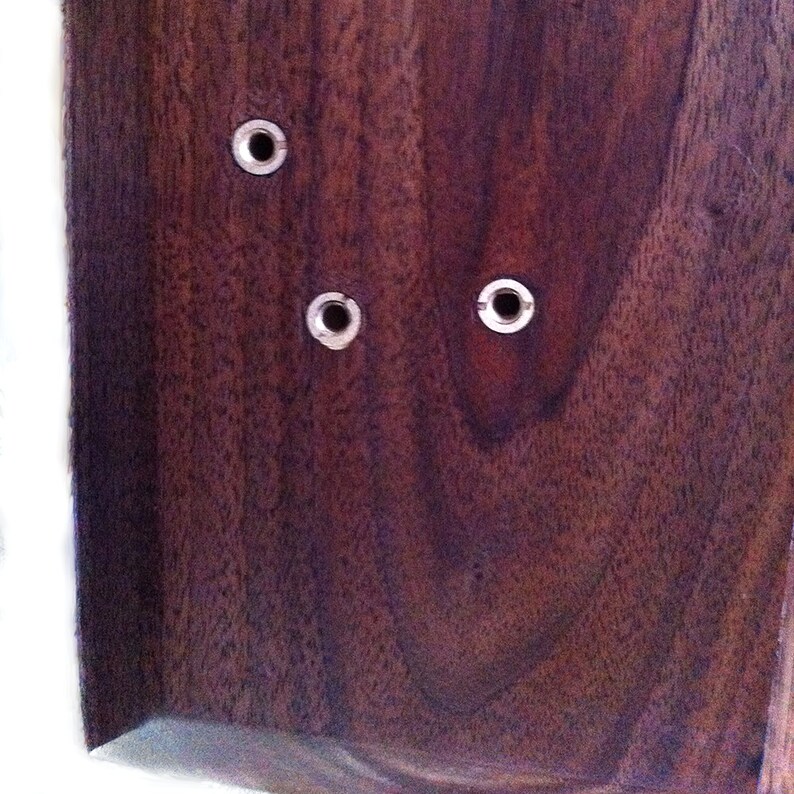 May include: Close-up of a dark brown wooden surface with three silver metal grommets.