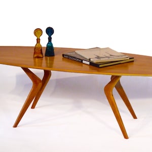 May include: A mid-century modern coffee table with a light wood top and unique, angled legs. The table is decorated with two glass bottles and a stack of books.