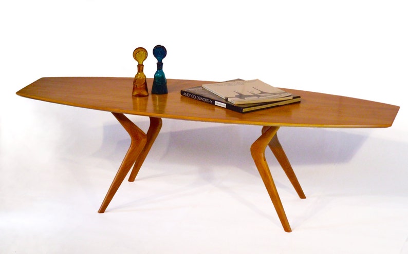 May include: A mid-century modern coffee table with a light wood top and unique, angled legs. The table is decorated with two glass bottles and a stack of books.