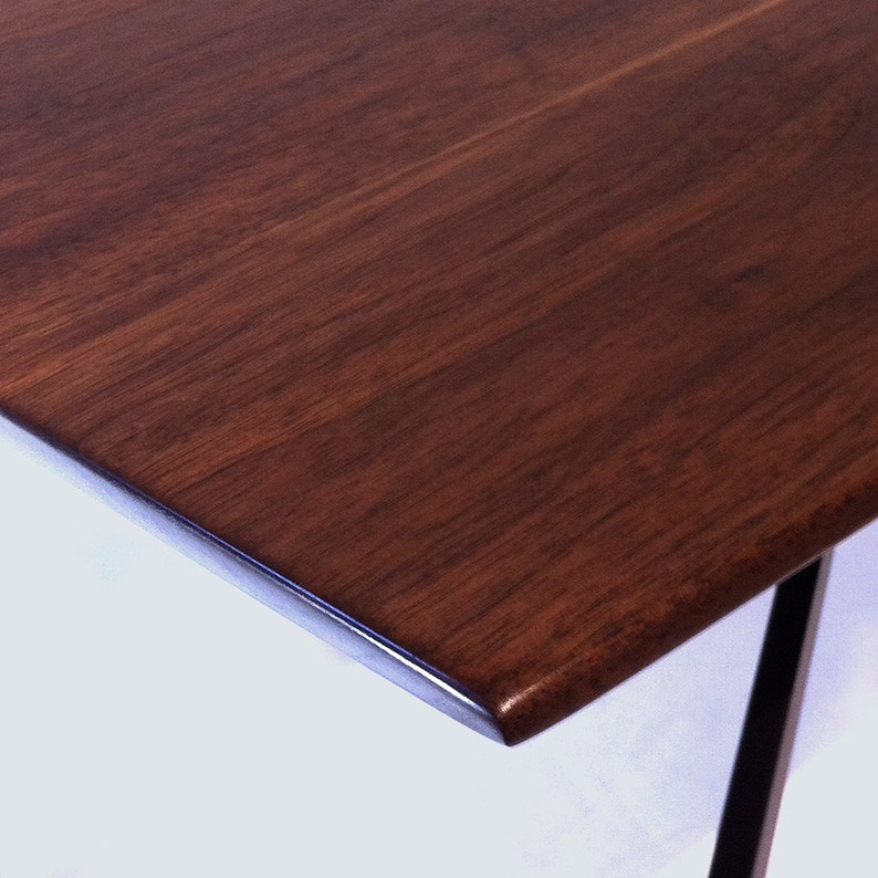 May include: Close-up of a dark brown wooden table top with a smooth, polished finish. The table top has a slightly rounded edge.