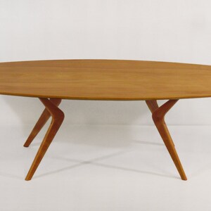 May include: A wooden coffee table with a long, oval-shaped top and four unique, curved legs.