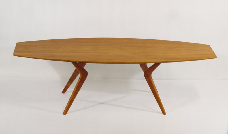 May include: A wooden coffee table with a long, oval-shaped top and four unique, curved legs.
