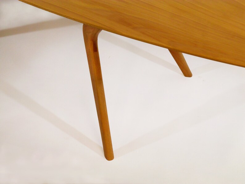 May include: Close-up of the legs of a wooden table. The table has a light brown finish and the legs are slender and tapered. The legs are angled slightly inward.