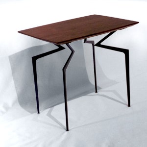 May include: A dark wood table with a unique, geometric, black metal base. The table has a rectangular top and four legs that are angled and connected in a zig-zag pattern.