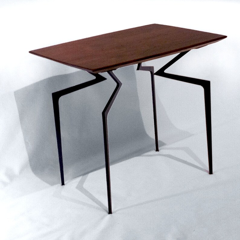 May include: A dark wood table with a unique, geometric, black metal base. The table has a rectangular top and four legs that are angled and connected in a zig-zag pattern.