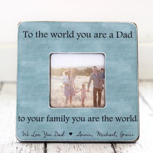 May include: Square, light blue picture frame with a family photo. The frame has the text "To the world you are a Dad, to your family you are the world." and "We Love You Dad Annie, Michael, Gracie."