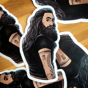Puede incluir: Una pegatina con una ilustración detallada de una persona con el pelo largo y negro y barba. La persona lleva una camisa negra y tiene tatuajes en los brazos. La pegatina está impresa en papel blanco.