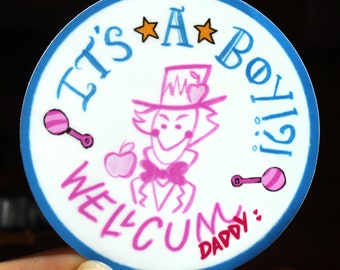 Puede incluir: Una pegatina redonda blanca con un borde azul. La pegatina tiene un personaje de dibujos animados rosa con un sombrero y sosteniendo una manzana. El texto en la pegatina dice "¡Es un niño!" y "Bienvenido Papá".