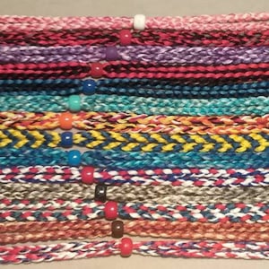 May include: A collection of colorful braided cords with different patterns and names, including pink multi, red/gray/black multi, purple multi, firefighter, blue line law, turquoise multi, flame multi, blue/yellow twist, blue/aqua multi, stars and stripe, gray multi, stars and twist, brown multi stripe, and red/white/blue multi.