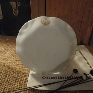 May include: A white porcelain plate with a scalloped edge and a floral design in the centre. The plate is sitting on a hessian surface.
