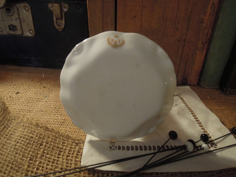 May include: A white porcelain plate with a scalloped edge and a floral design in the centre. The plate is sitting on a hessian surface.