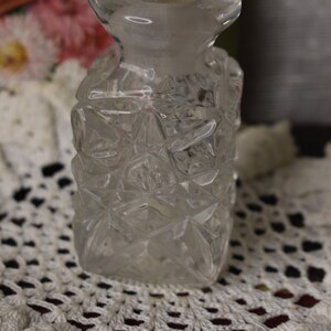 May include: A clear glass bottle with a diamond-shaped pattern. The bottle is sitting on a white crocheted doily.