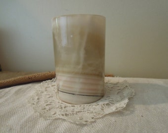 May include: A cylindrical, white and brown, alabaster vase with a swirling pattern.