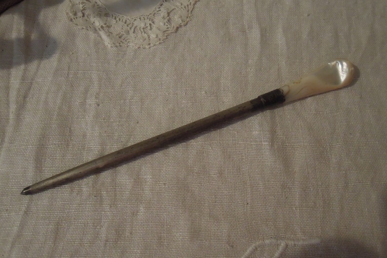 May include: A long, thin, silver-colored metal knitting needle with a white, pearlescent handle.