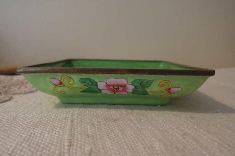 Op de afbeelding: Een vierkante, groene cloisonn&eacute;-schotel met een bloemenmotief. De schotel heeft een gouden rand en is versierd met roze en gele bloemen en groene bladeren.