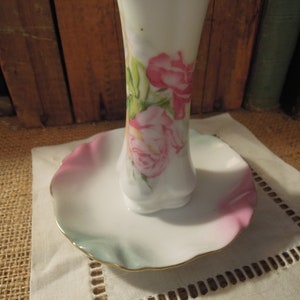May include: A white porcelain ring holder with a ruffled edge and a floral design featuring pink roses and green leaves.