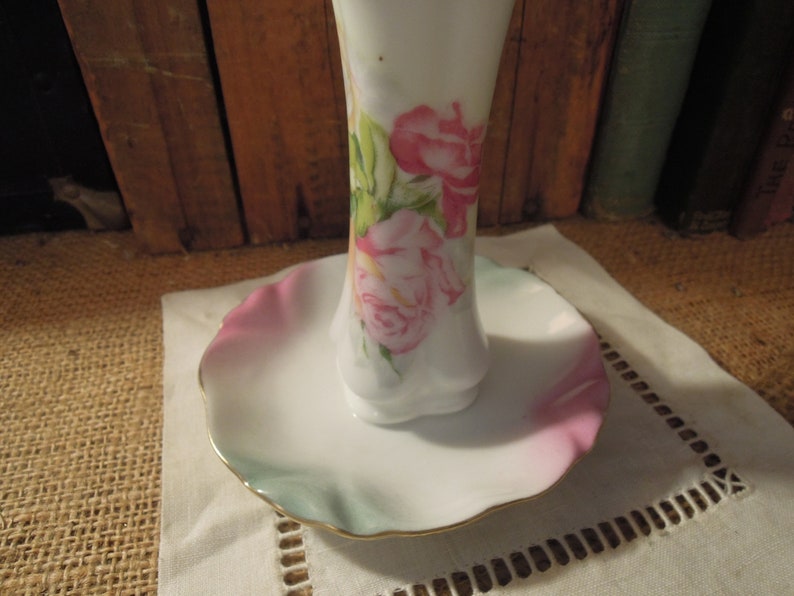 May include: A white porcelain ring holder with a ruffled edge and a floral design featuring pink roses and green leaves.