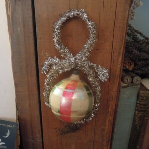 May include: A vintage glass Christmas ornament with red, green, and white stripes. The ornament is decorated with silver tinsel.